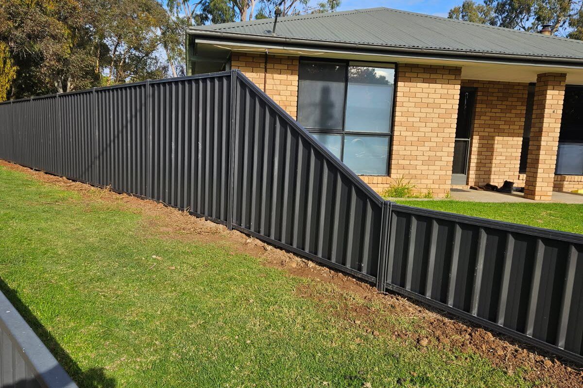 Black Colorbond fence stepping down a sloped garden beside a brick house